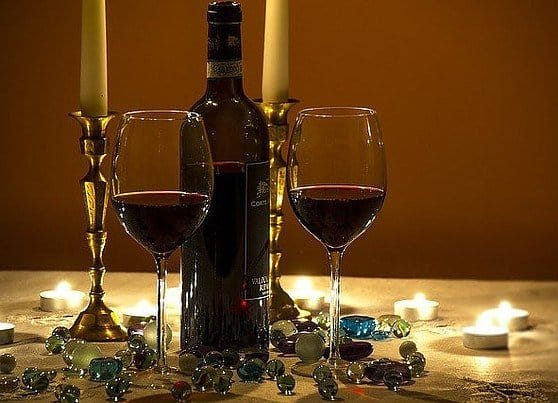 two candles,a bottle of redwine and two filled wine glasses on a table, covered with blue cristals