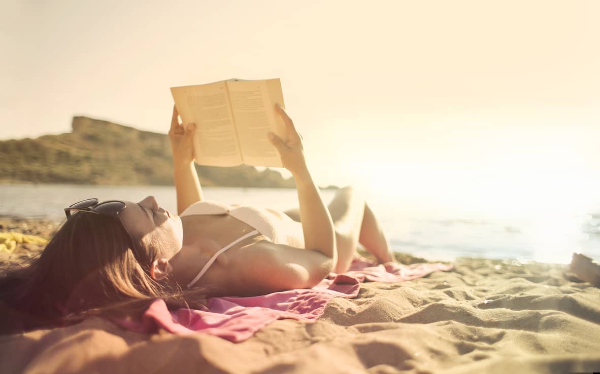 a woman reading a book lying at the beach