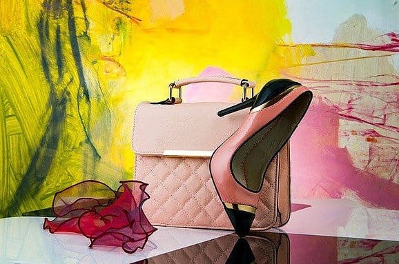 A pink colored high heel shoe, a handbag and a scarf on a table
