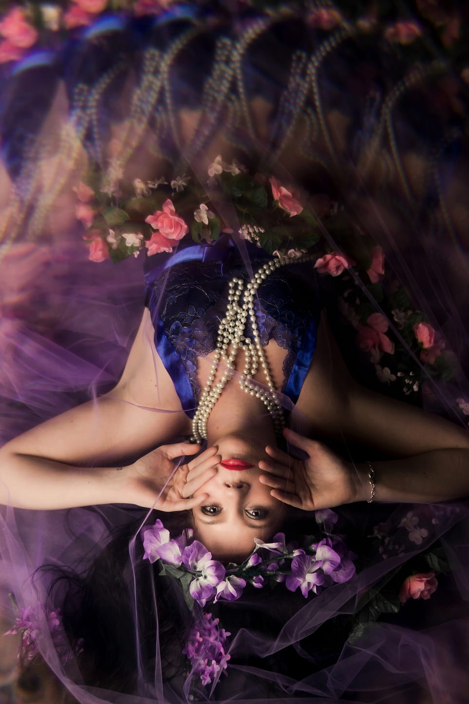 A beautiful woman lying between roses and purple flowers