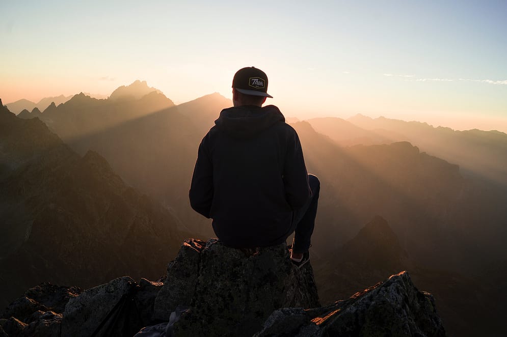 a young man sitting high up in the mountains at sun set
