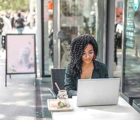 woman with curly black hair sitting in a coffee shop working on her laptop