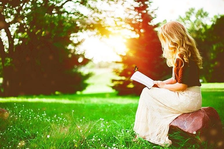 a woman sitting and reading in a park by sunshine