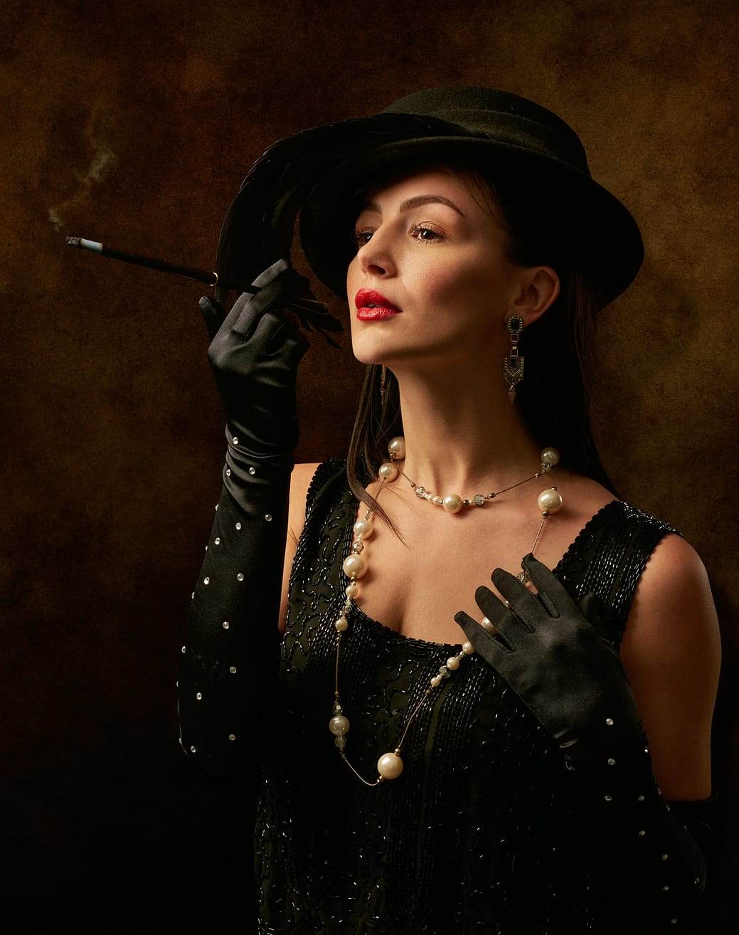 woman in black dreaa and black gloves, black hat, with pearls and earings
