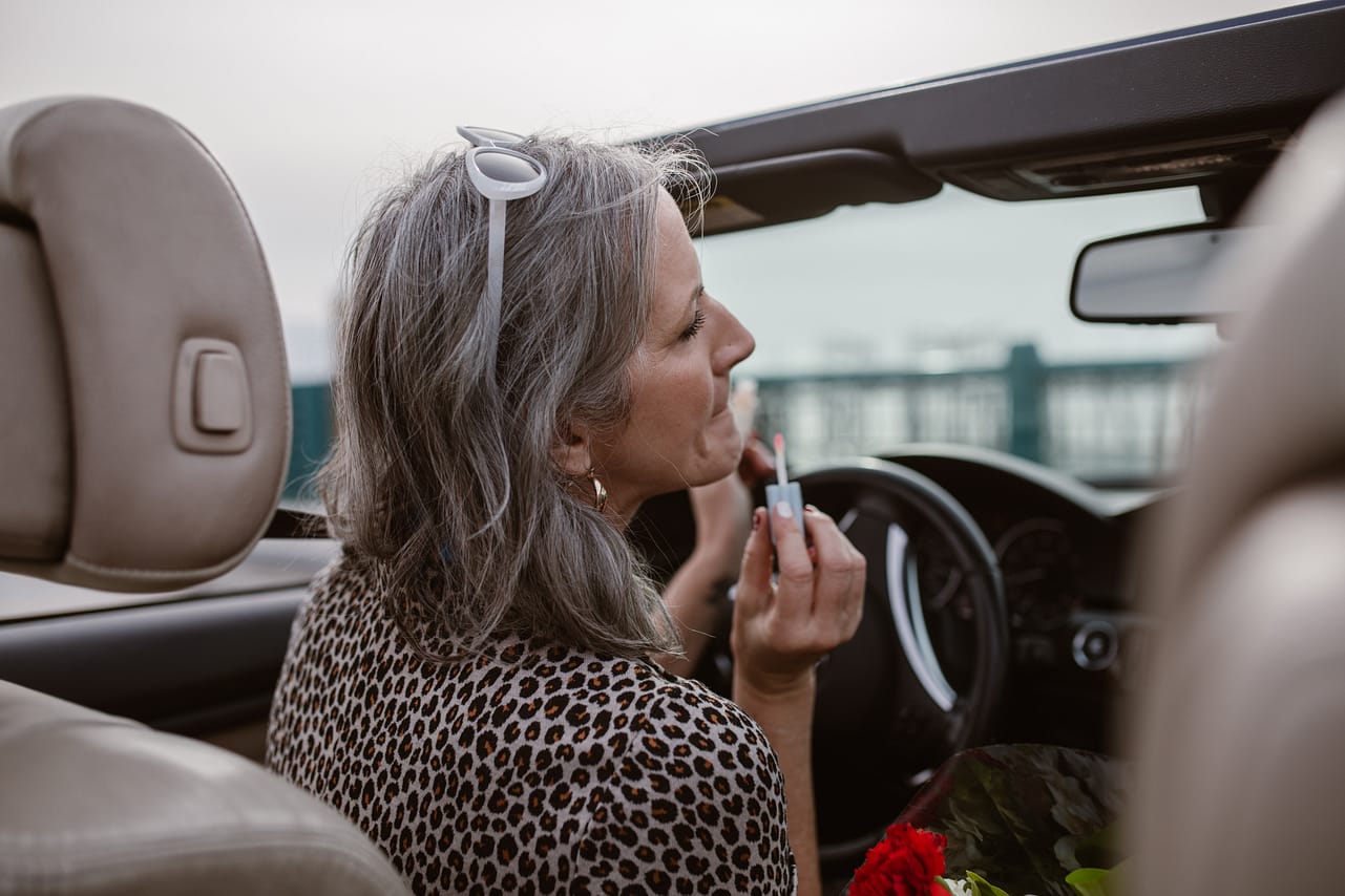 stylish woman in her Cabrio, using lipstick
