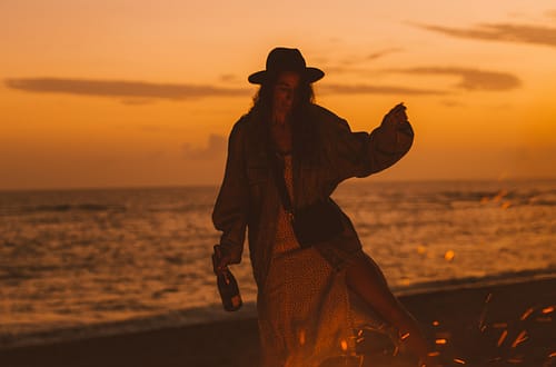 a woman dancing around a fire at the beach