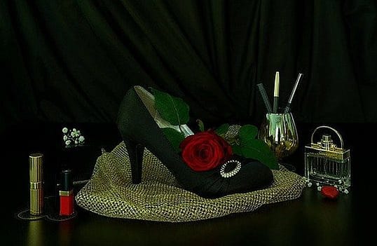 green elegant shoe with a red rose, and a pearl broche, makeup pencils, lipstick, flacon with perfume on a golden colored material