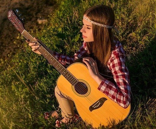 A hippy woman sitting in the grass playing guitar