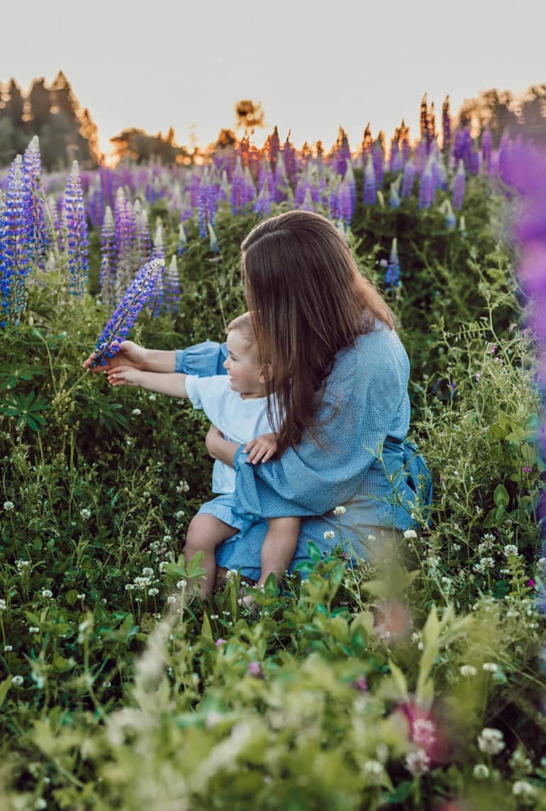 a mother with her baby sitting in a field of wild flowers